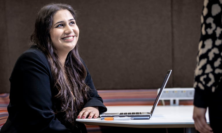 four students sitting around the table and looking on computer happily