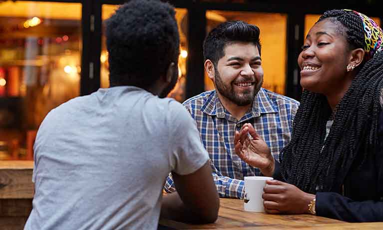 Three students socialising at a table outside a bar