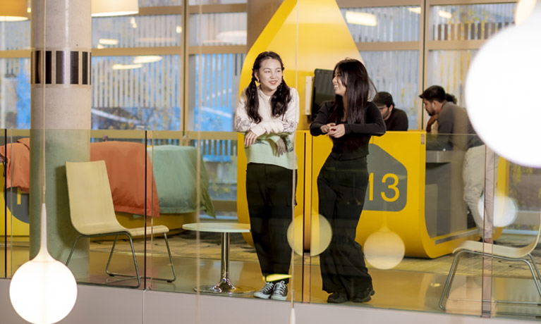 two female chinese students leaning against glass wall in the HUb