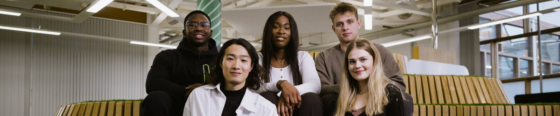 Group of 5 students sitting on wooden steps in an inside shared space