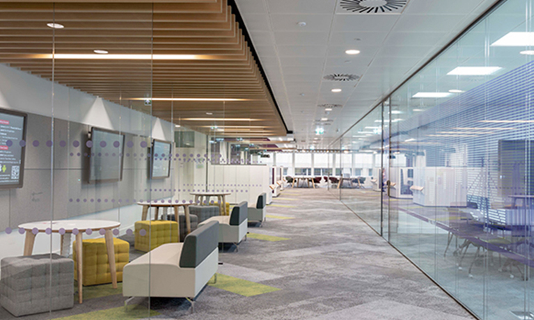 Hallway with glass walls through which tables and sofas are visible