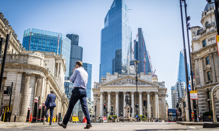 Two men on mobile phones walking in front of the Bank of England