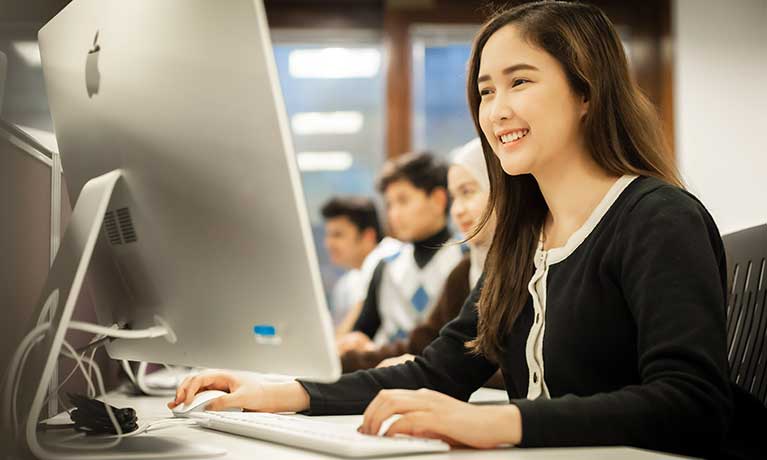 An undergraduate student smiling as she uses a mac on campus.