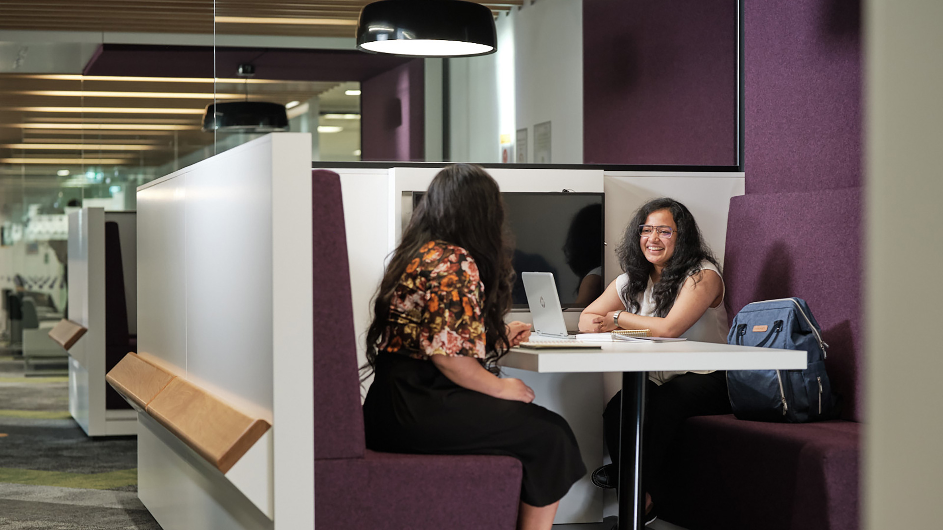 Two females chatting at a table looking into a laptop