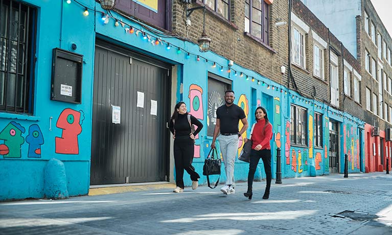 3 young people walking down a street with colourful shop fronts