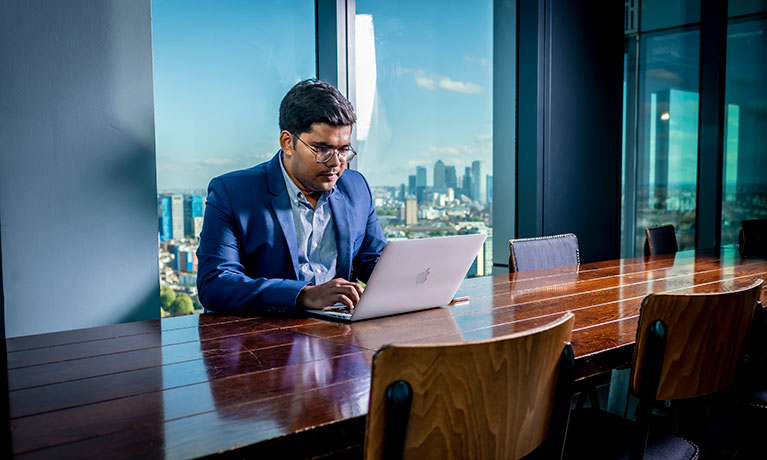 Student in a boardroom using a laptop with London skyline behind them