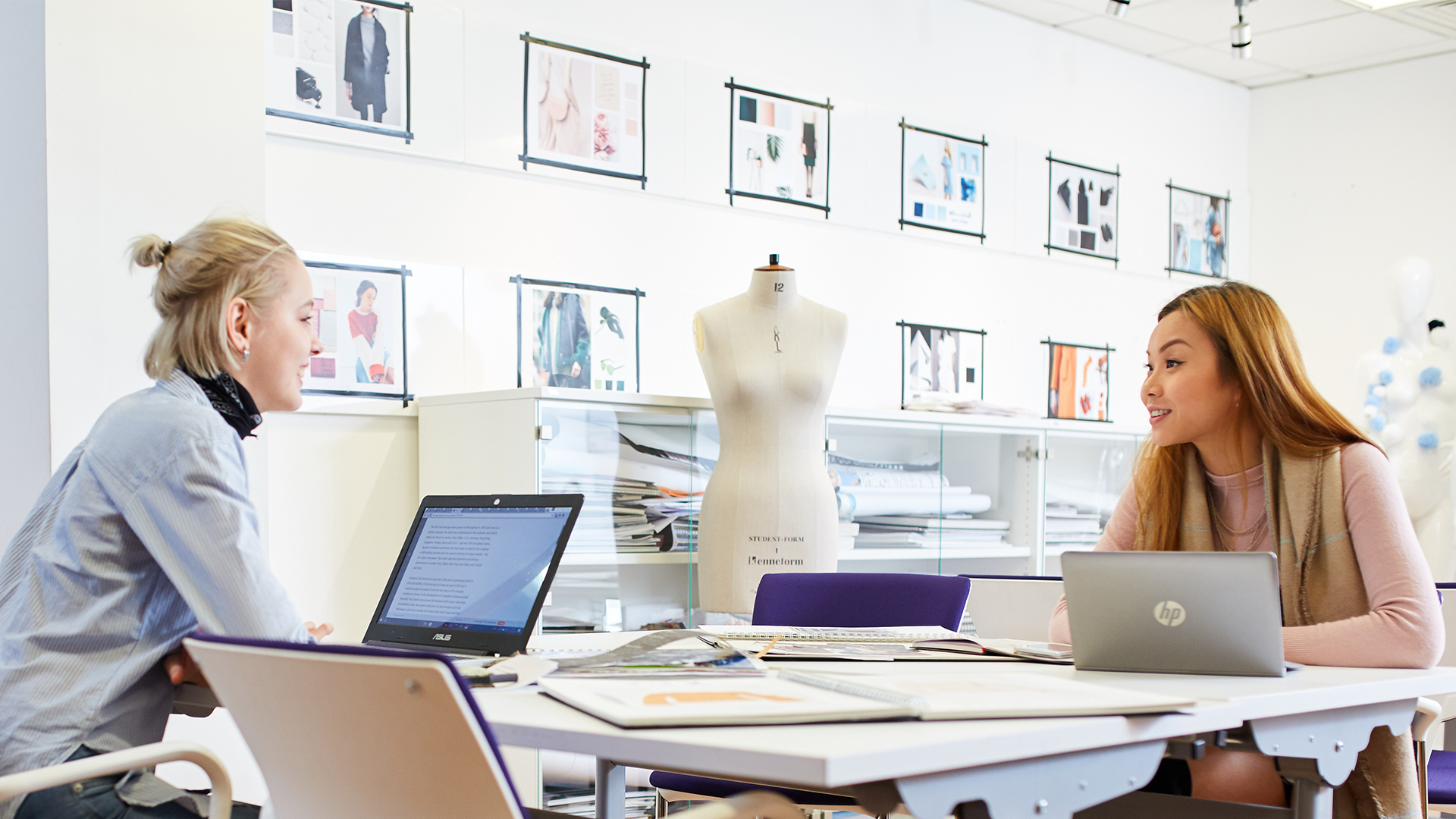 Two ladies in a fashion shop looking at designs on laptops in a bright studio
