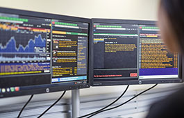 Two computer screens showing data graphs and coding