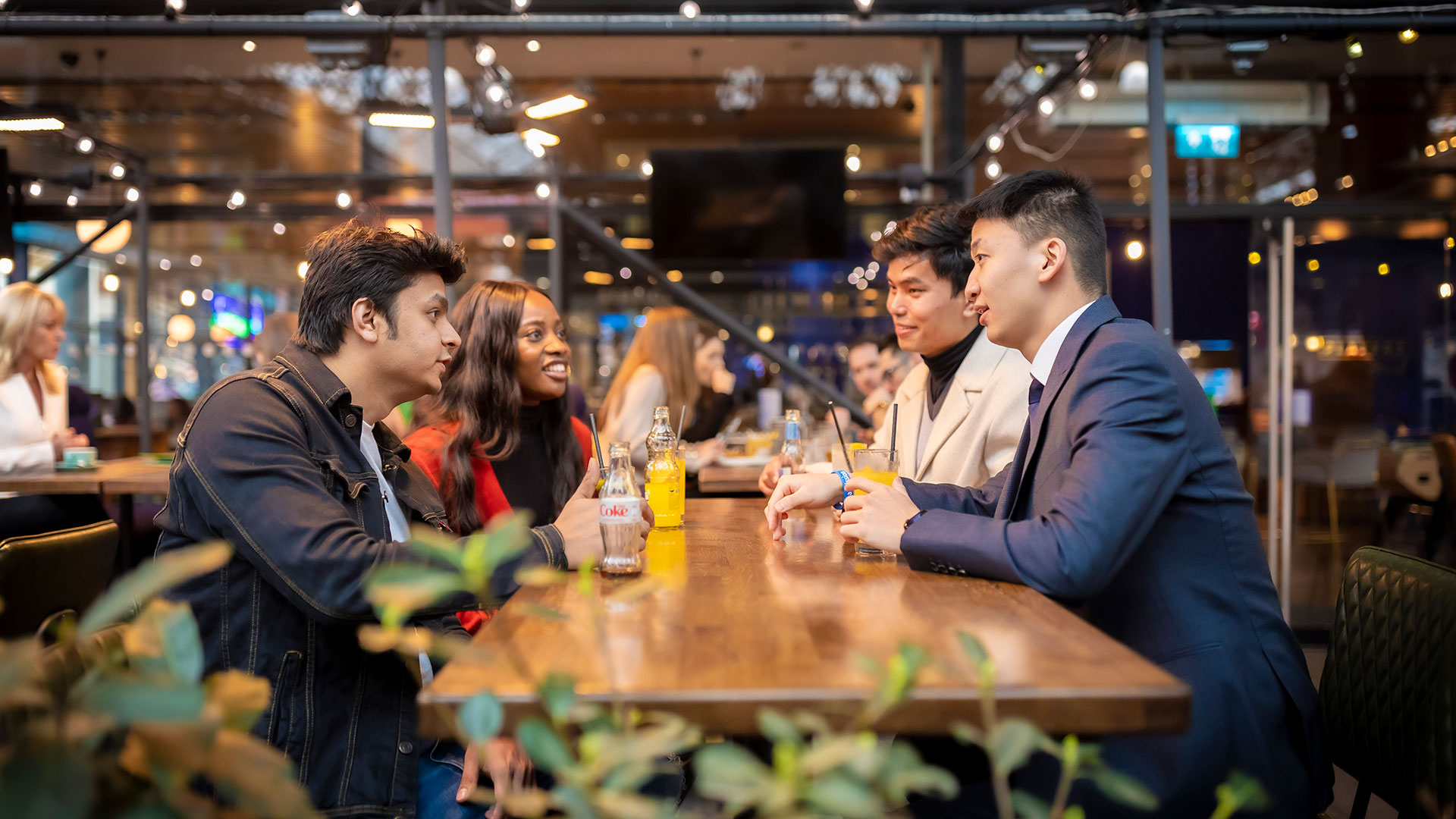 Four young people talking to each other over drinks in a busy bar