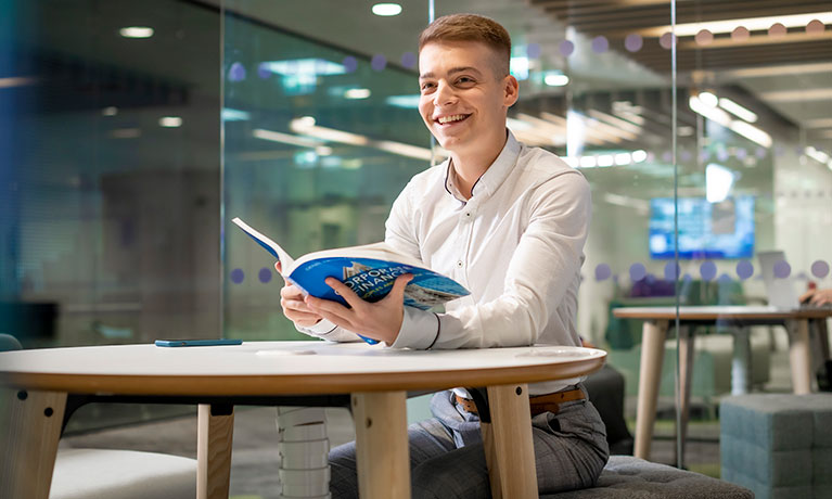 Male student sat at a desk holding a book 