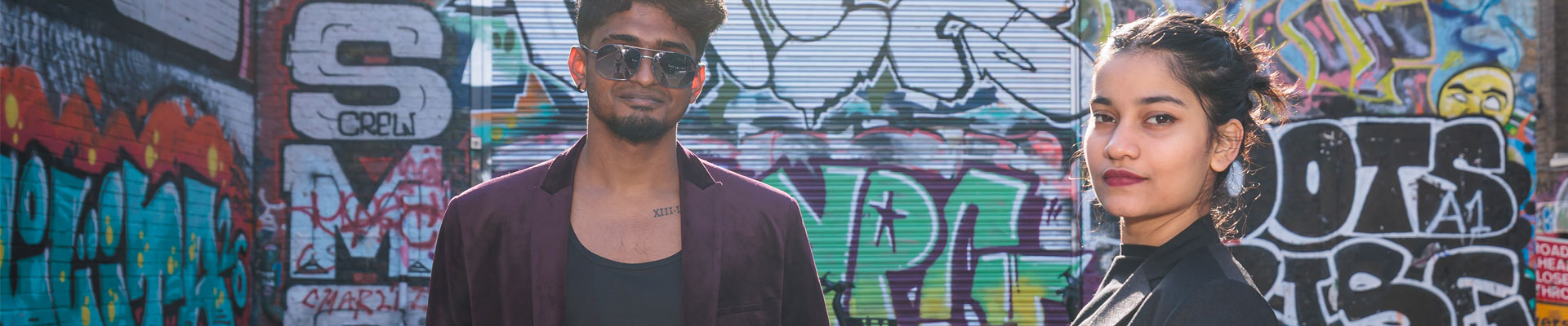 Two students looking at the camera in front of a wall covered in street art