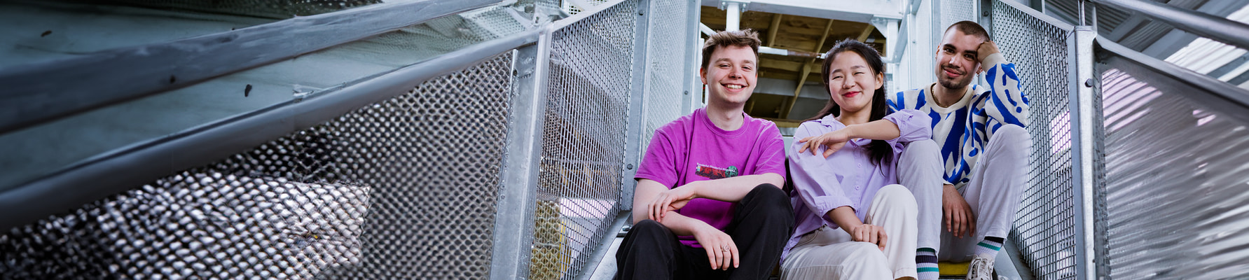 Three students sat on a staircase looking down smiling