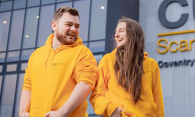 Two students in CU Scarborough jumpers facing each other laughing