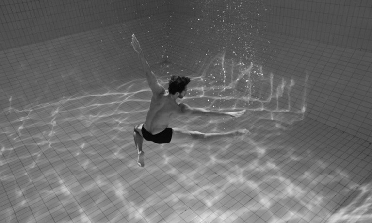 Black and white photograph of a man swimming underwater in a swimming pool