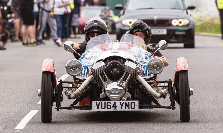 A classic car on the road with spectators behind