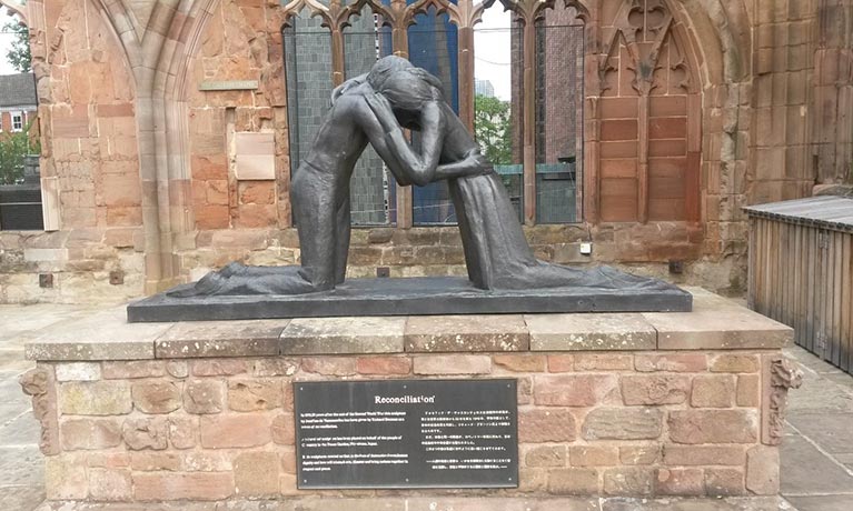Statue of two people hugging on a pedestal with the title reconciliation