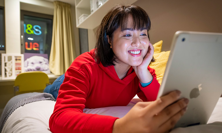 Girl looking at a tablet lying on her bed 