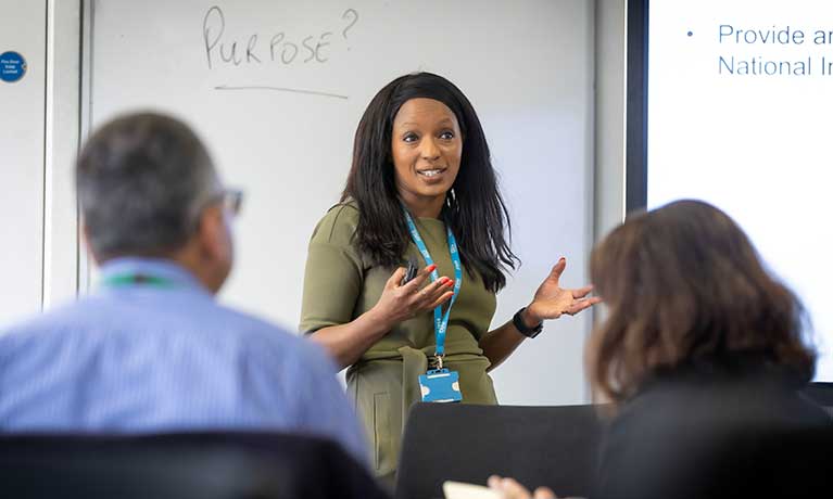 A woman standing in front of people in a room talking