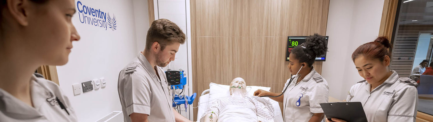 Nursing students in a mock hospital ward, stood around a manikin in a hospital bed