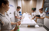 Nursing students around a simulation mannequin in a hospital bed