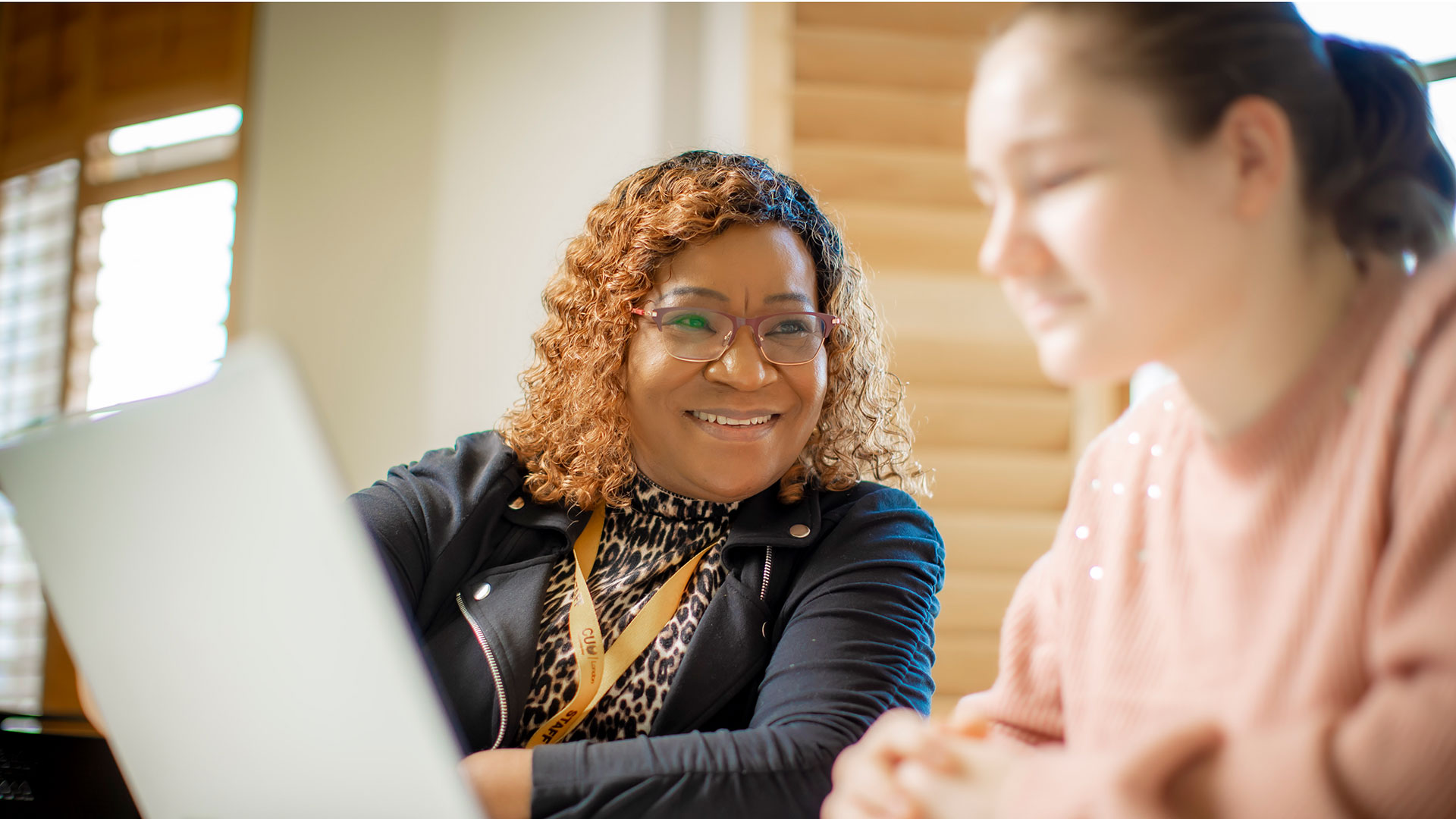 A smiling lecturer looks at a student who is concentrating on her laptop