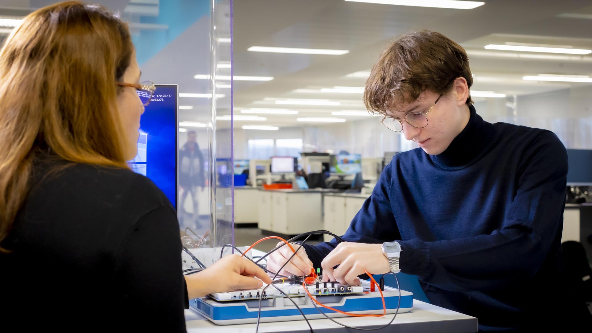 Student using a circuit board with a tutor watching him.