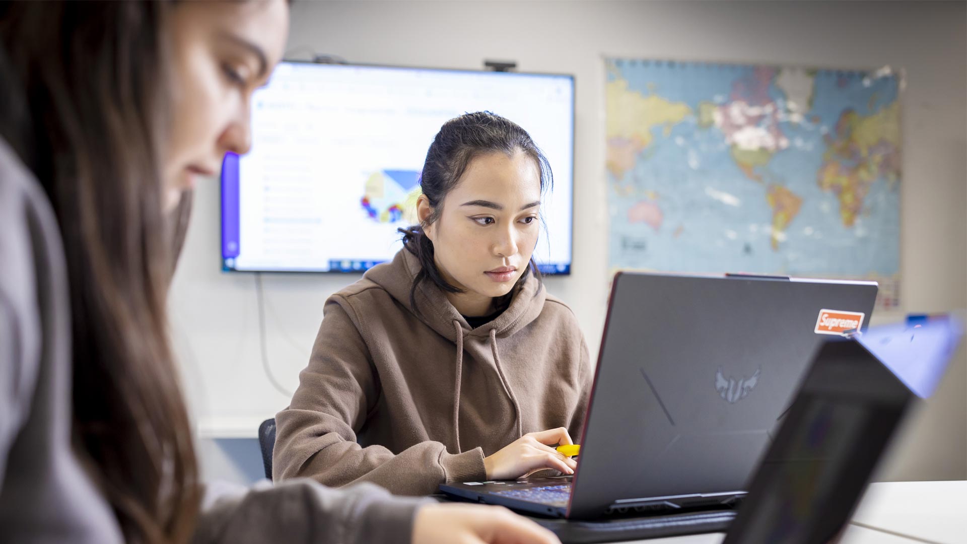 Two tourism students working on laptops in a classroom.