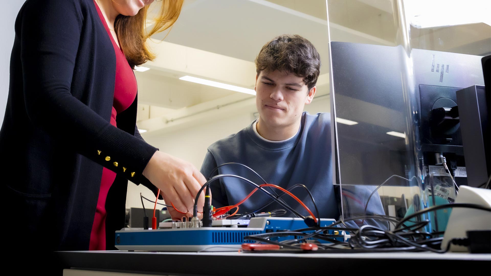A tutor helping a studet use electrical engineering equipment.