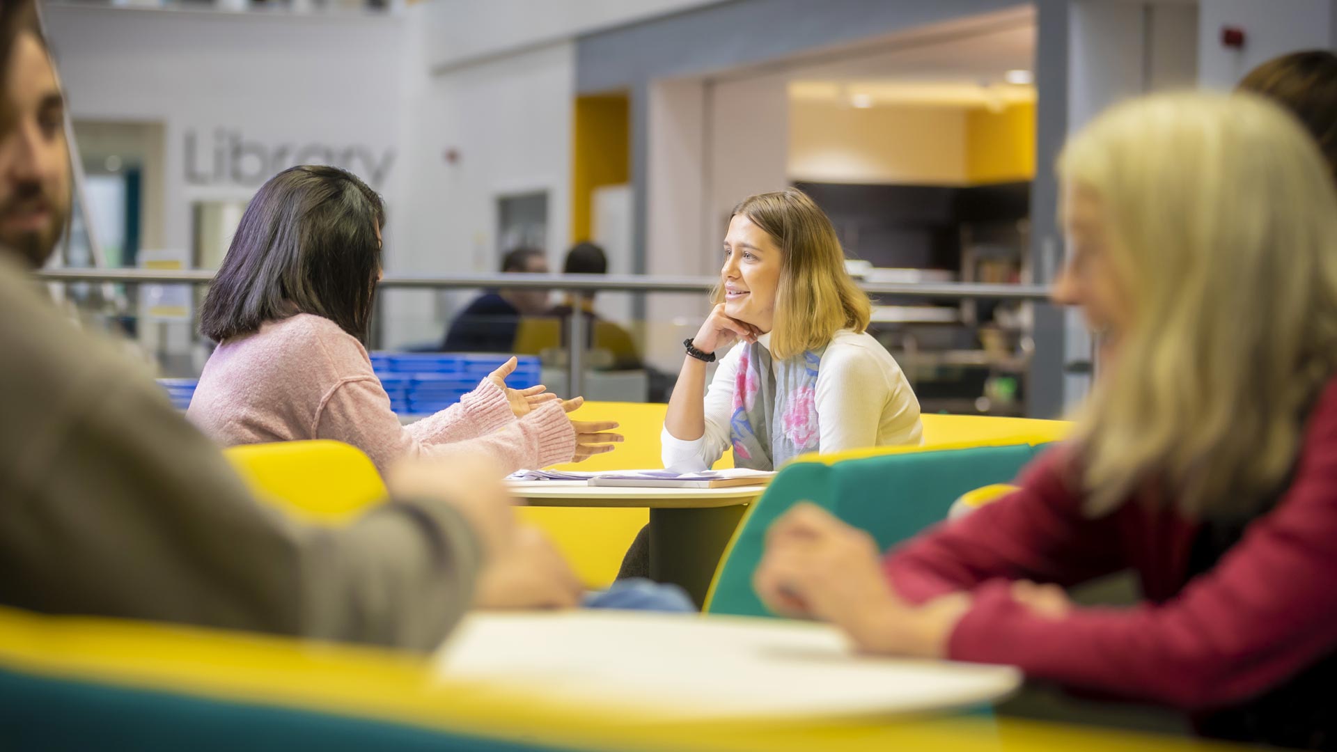 Students chatting in a social space with other students sat around them.