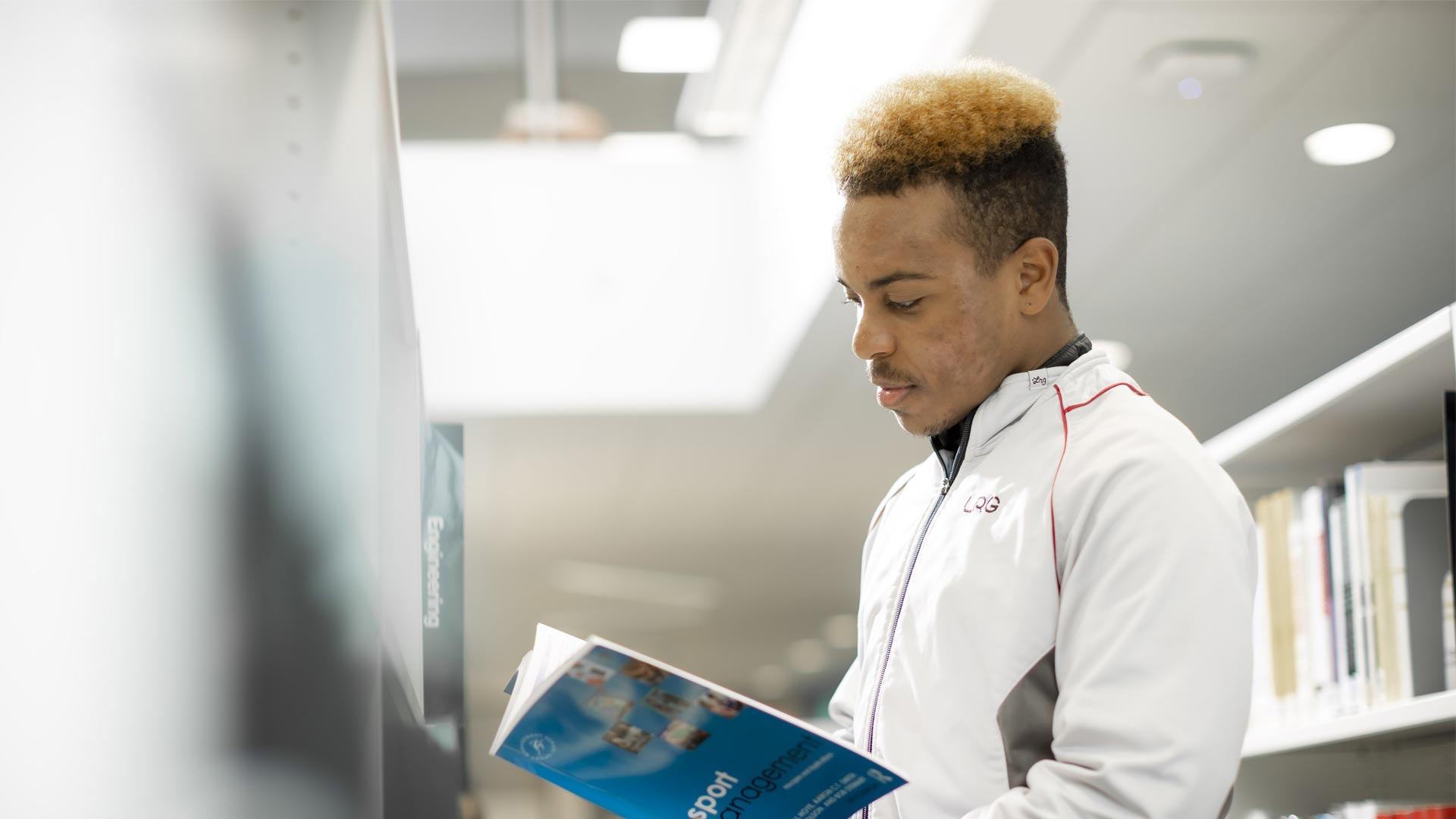 Sport student in sportswear reading a textbook in the library.
