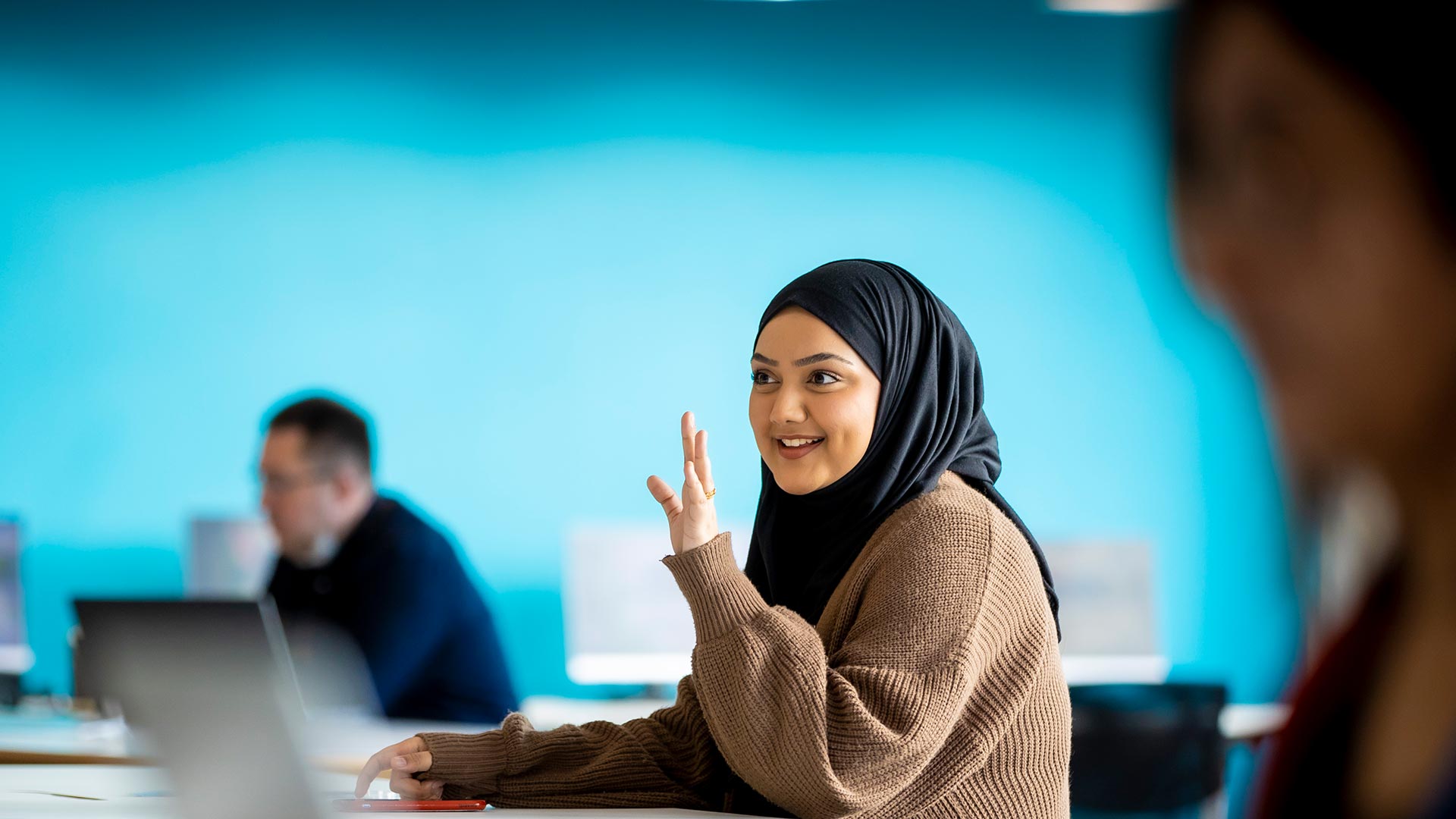Female student sat in a class room with her hand raised
