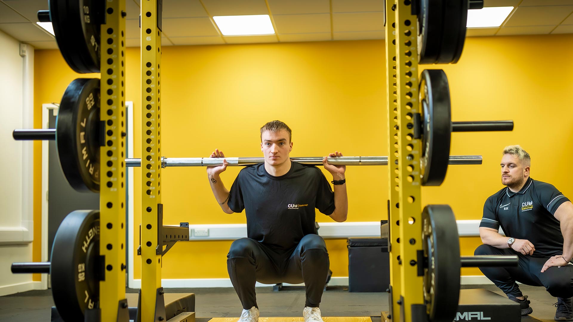 Male student weightlifting next to a coach