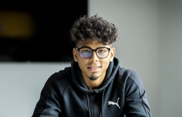 A student sitting in a classroom looking confidently into the camera.