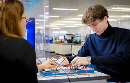 Student using a circuit board with a tutor watching him.