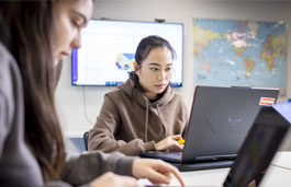 Two tourism students working on laptops in a classroom.