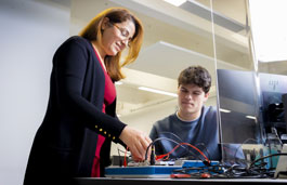 A tutor helping a studet use electrical engineering equipment.