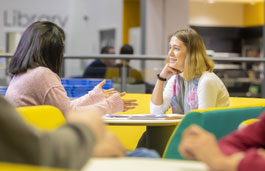 Students chatting in a social space with other students sat around them.