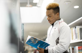 Sport student in sportswear reading a textbook in the library.