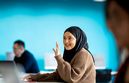 Female student sat in a class room with her hand raised