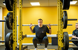 Male student weightlifting next to a coach