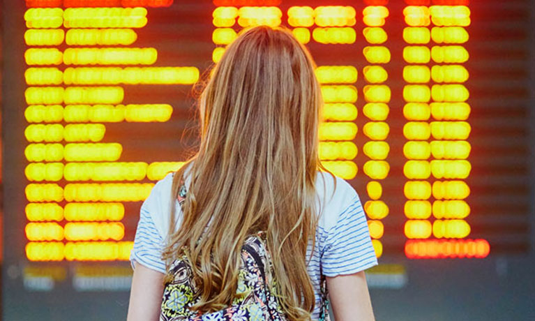 Student with a backpack looking at an airport departures board