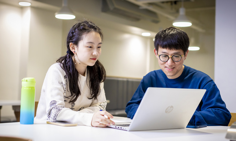 Two international students working on a laptop in a study space.