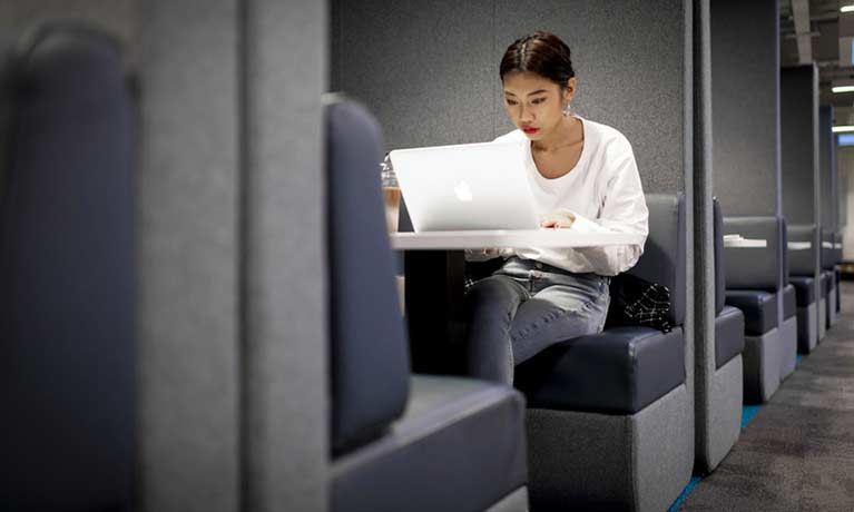 Female student in a booth on her laptop looking serious