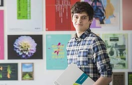 Smiling student standing in front of a wall covered in art 