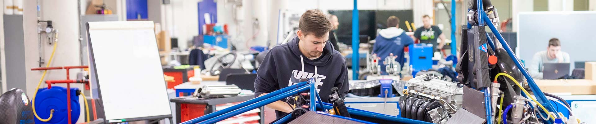 Smiling student sitting in motorsport car with another student looking on