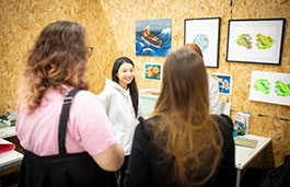 Smiling student standing in front of a wall covered in art 