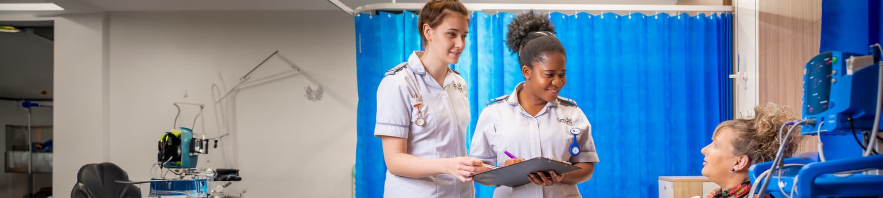 Two student nurses talking to a mock patient in a mock hospital bay