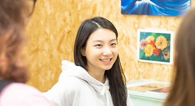 A smiling student with artwork behind her talks to visitors