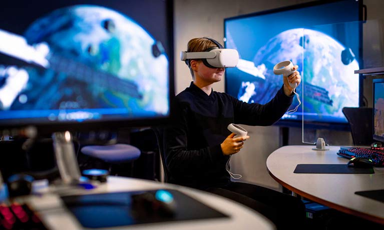 Student wearing in a VR set using controllers in a computer lab