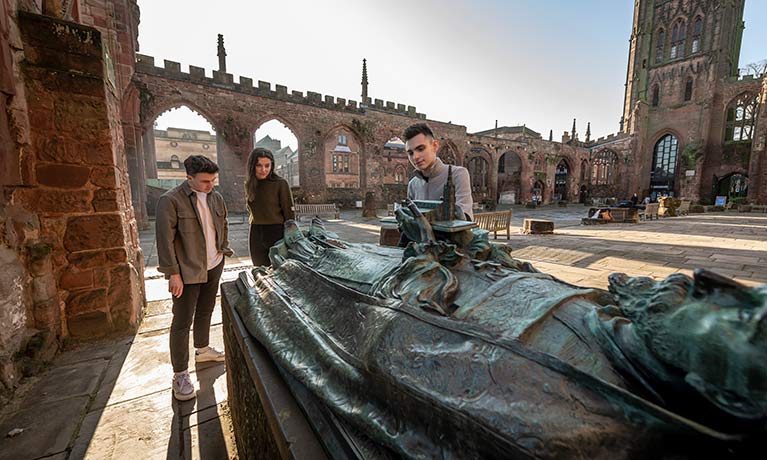 Three students in ruins of Coventry Cathedral looking at burial memorial